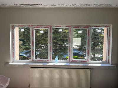 Yeni PVC doğrama takıldı, koruyucu bantları üzerinde. Tek parça beyaz mermer denizlik ve altında uzun panel radyatör yerine oturdu.