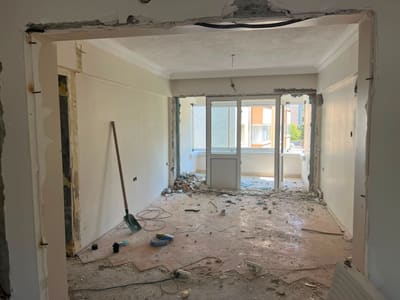 Yıkımın ilk günü. Balkon hâlâ ayrı: ortada alt panelli balkon kapısı, iki yanında pencere. Kapı çevresindeki duvarın üst bandı sökülmüş, lento açığa çıkmış.